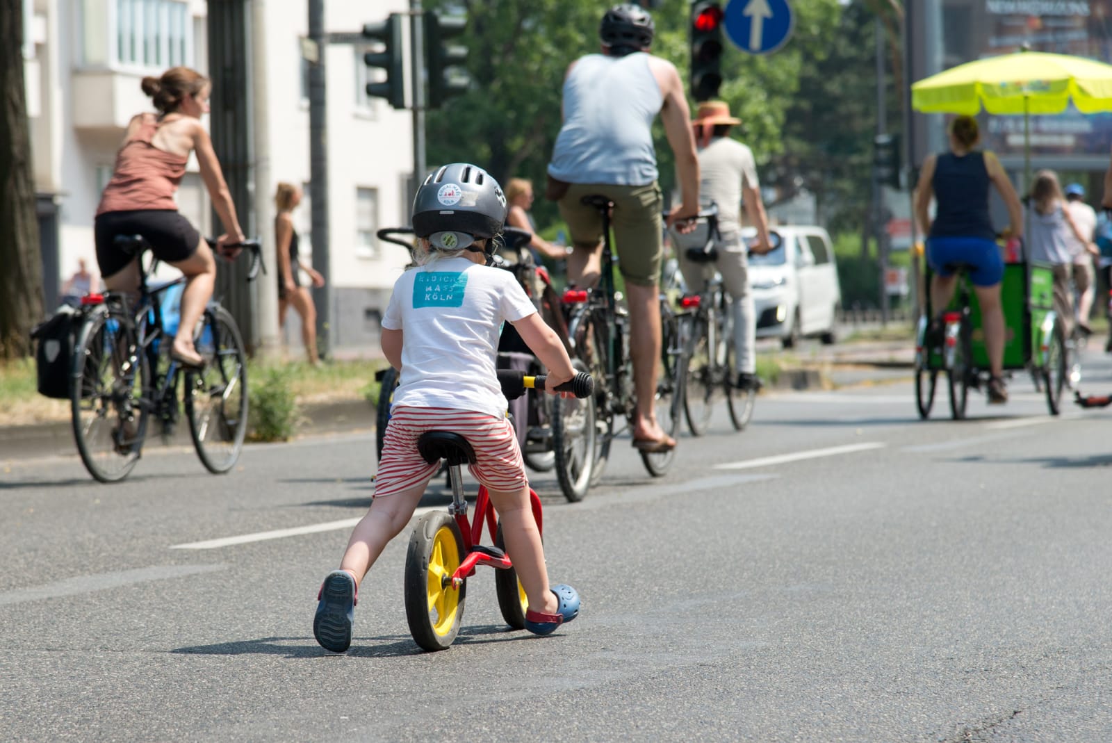 Kind auf Laufrad, im Hintergrund einige Fahrradfahrer:innen